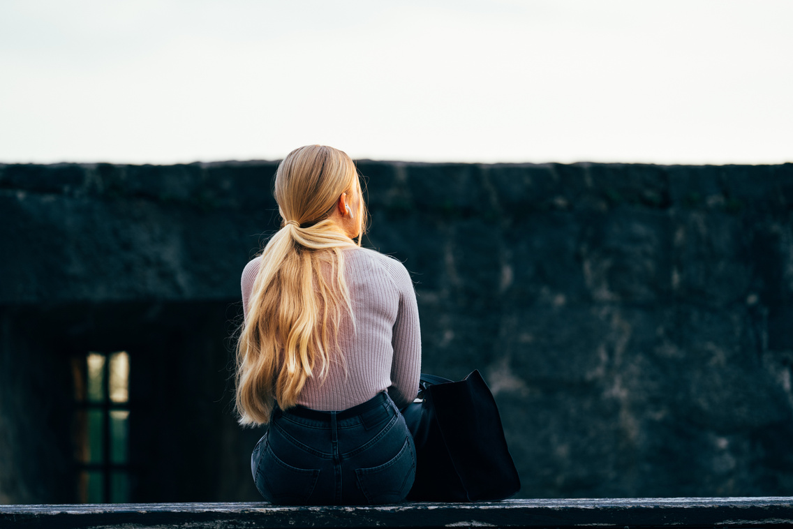 Woman in White Long Sleeve Shirt and Black Pants Sitting on Gray Concrete Wall